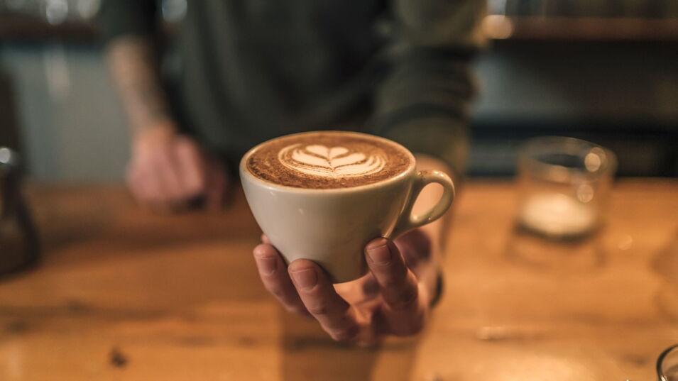 Ein Cappuccino mit Milchherzen wird dem Betrachter gezeigt und überreicht.