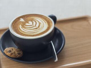 Barista Cappuccino serviert in einer schwarzen Tasse auf einem Holztablett