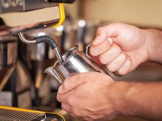 Barista hält Milchkaennchen an eine Dampflanze