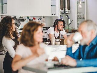 Kellnerin bringt Kaffee und ein Barista freundlicher Barista ist im Hintergrund