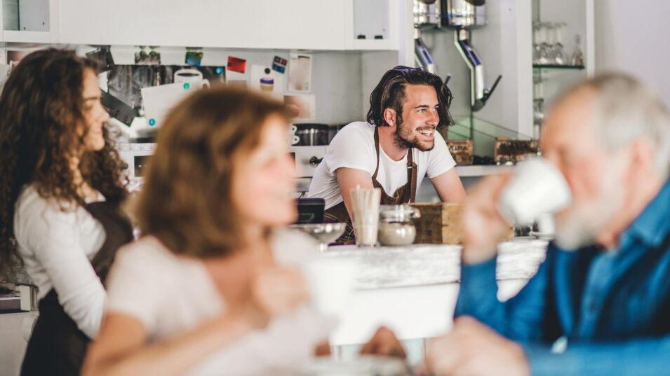 Kellnerin bringt Kaffee und ein Barista freundlicher Barista ist im Hintergrund