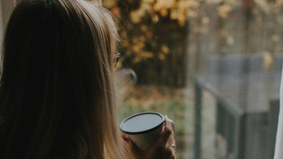 Frau hält eine Tasse in der Hand und schaut aus dem Fenster