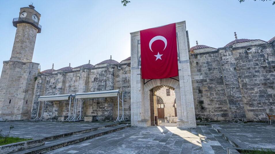 Historisches Gebäude mit einer großen türkischen Flagge über dem Eingang und einem Uhrturm im Hintergrund.