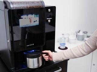 Frau stellt Kanne unter Kaffeeautomaten