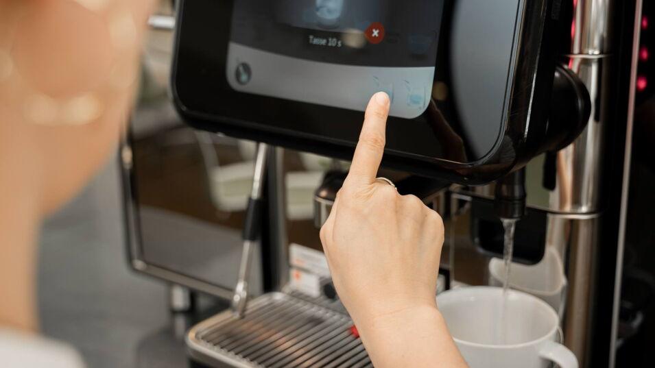 Eine Person bereitet Tee zu, während heißes Wasser aus einem Kaffeevollautomaten in eine Tasse läuft