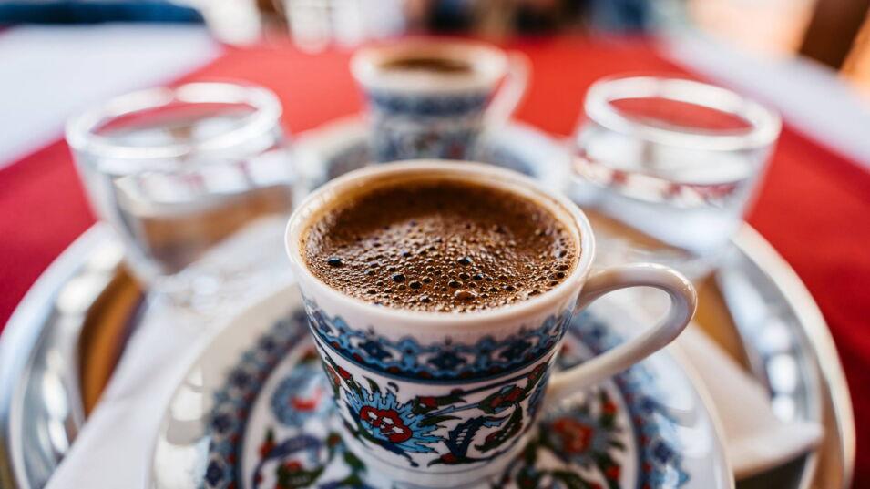 Traditioneller türkischer Kaffee in einer verzierten Tasse, serviert mit einem Glas Wasser auf einem silbernen Tablett.