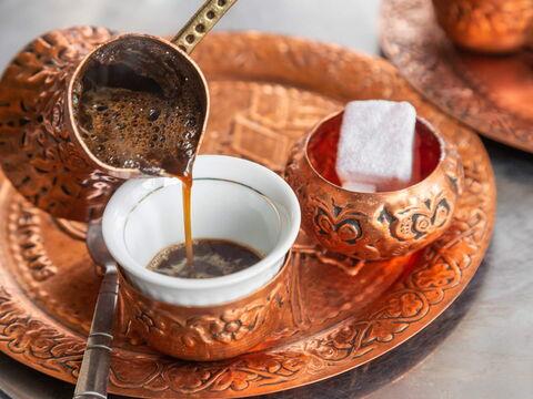 Traditioneller türkischer Kaffee wird in eine verzierte Tasse aus einem Kupfergefäß gegossen, mit einem Stück Zucker auf dem Tablett.