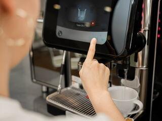 Eine Person bereitet Tee zu, während heißes Wasser aus einem Kaffeevollautomaten in eine Tasse läuft