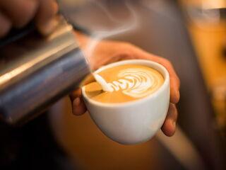 Barista gießt Milchschaum ein und bereitet Latte Art vor