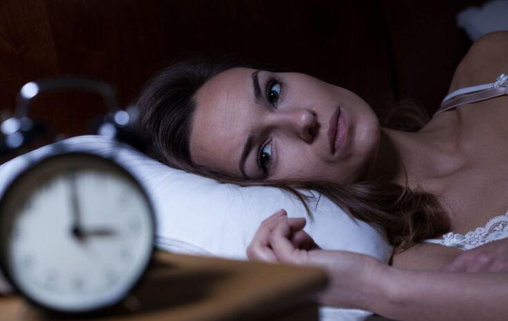 Frau liegt schlaflos im Bett und schaut auf den Wecker