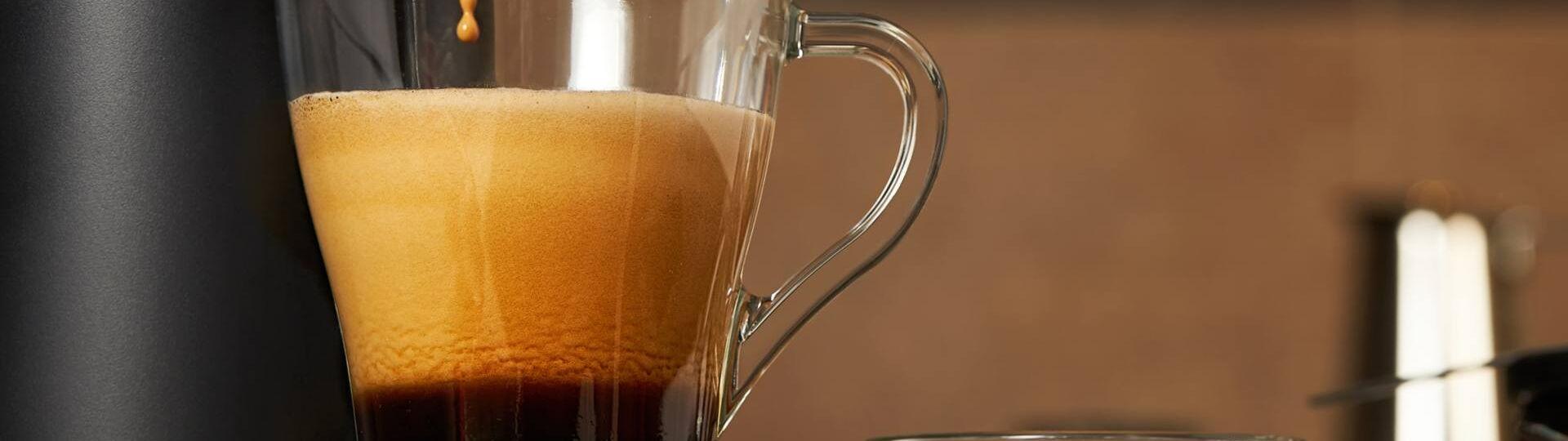 Ein transparentes Kaffeeglas fängt den frisch zubereiteten Kaffee, der aus einer Kaffeepadmaschine fließt.