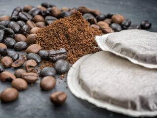 Eine Anordnung von Kaffeebohnen, Kaffeepads und gemahlenem Kaffee auf einem dunklen Hintergrund.