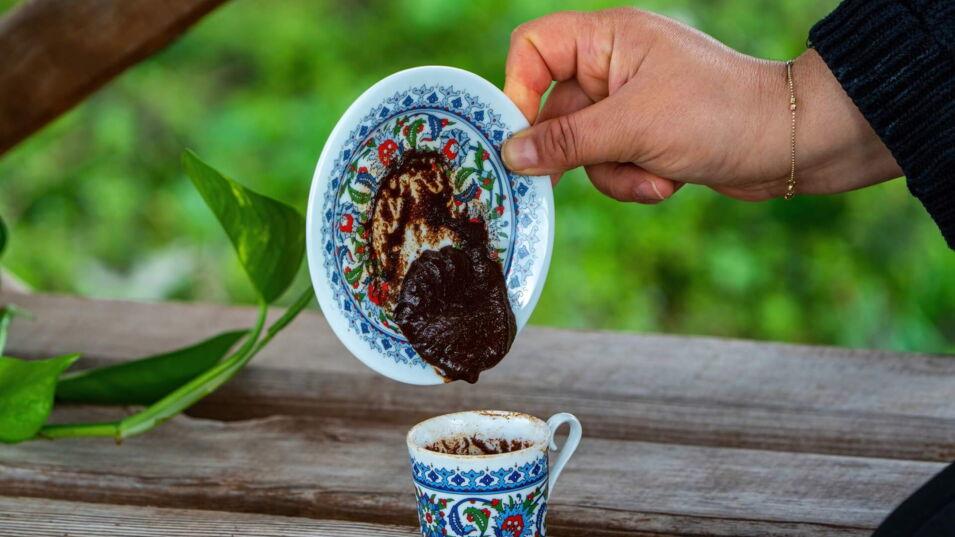 Person dreht eine traditionelle türkische Kaffeetasse um, um Kaffeesatz zu lesen.