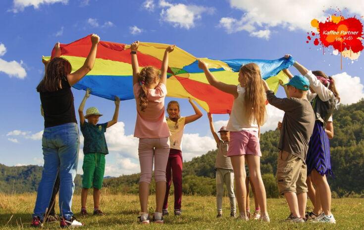 Kinder auf Wiese mit Regenbogentuch