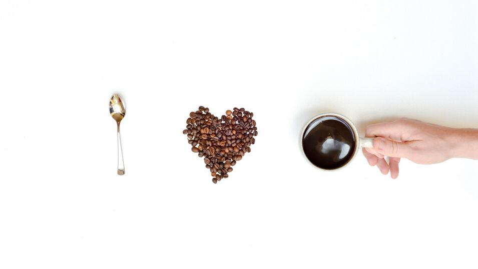 Loeffel Kaffeebohnen Herz und Tasse Kaffee in hand
