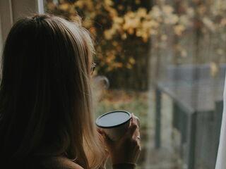 Frau hält eine Tasse in der Hand und schaut aus dem Fenster