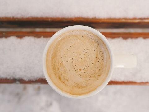 Kaffee mit Crema von oben auf einer verschneiten Parkbank