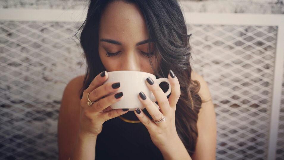 Frau hält eine weiße Tasse in der Hand und genießt den Kaffee