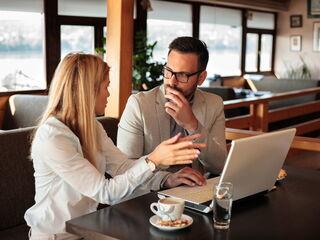 Zwei Geschäftspartner arbeiten an einem Laptop und unterhalten sich in einem Café