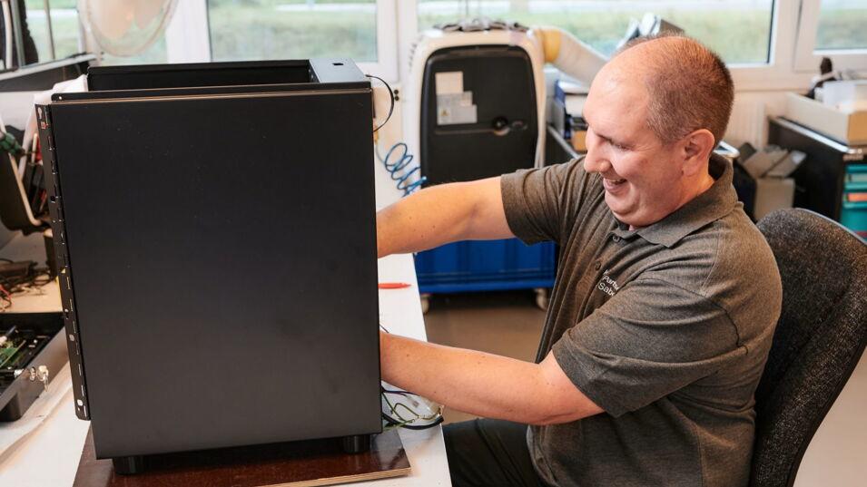 Techniker lächelnd bei der Instandsetzung eines Kaffeevollautomaten in einer Werkstatt mit technischem Equipment im Hintergrund