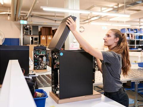 Fachkundige Technikerin klappt einen hochwertigen Kaffeevollautomaten in einer modernen Montagehalle auf.