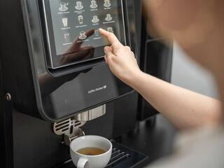 Eine Person wählt Heißwasser aus dem Auswahlmenü eines Kaffeevollautomaten und bereitet Tee zu