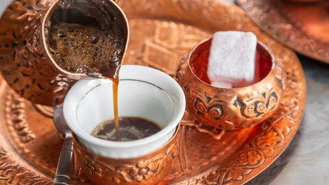 Traditioneller türkischer Kaffee wird in eine verzierte Tasse aus einem Kupfergefäß gegossen, mit einem Stück Zucker auf dem Tablett.