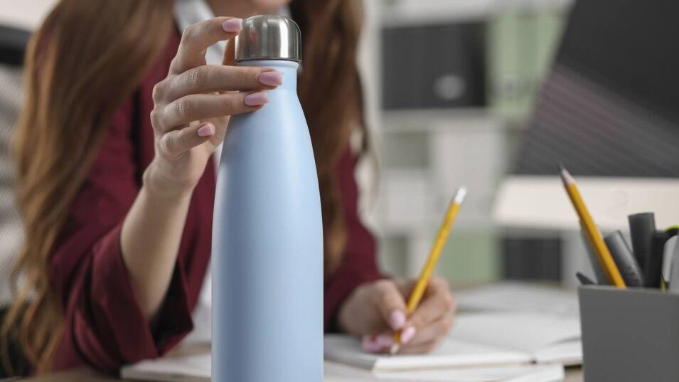 Frau hält eine wiederverwendbare Wasserflasche auf dem Schreibtisch im Büro.