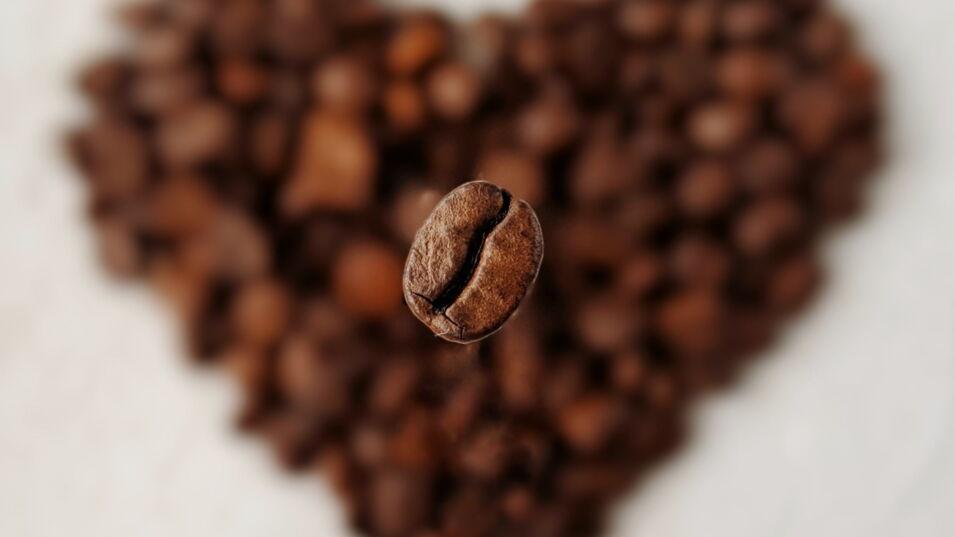Geröstete Kaffeebohne schwebt über einem Herz aus Kaffeebohnen, die unscharf im Hintergrund erkennbar sind