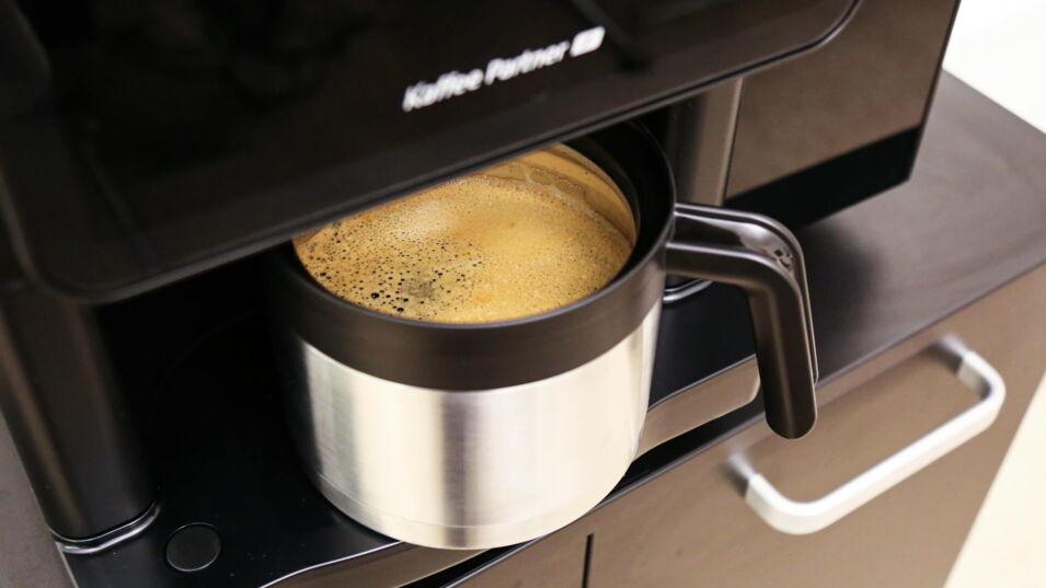 Edelstahl-Thermoskanne fängt gerade frisch gebrühten Kaffee aus einem Kaffeevollautomaten von Kaffee Partner auf, hervorgehoben durch die elegante Crema auf der Oberfläche des Getränks.