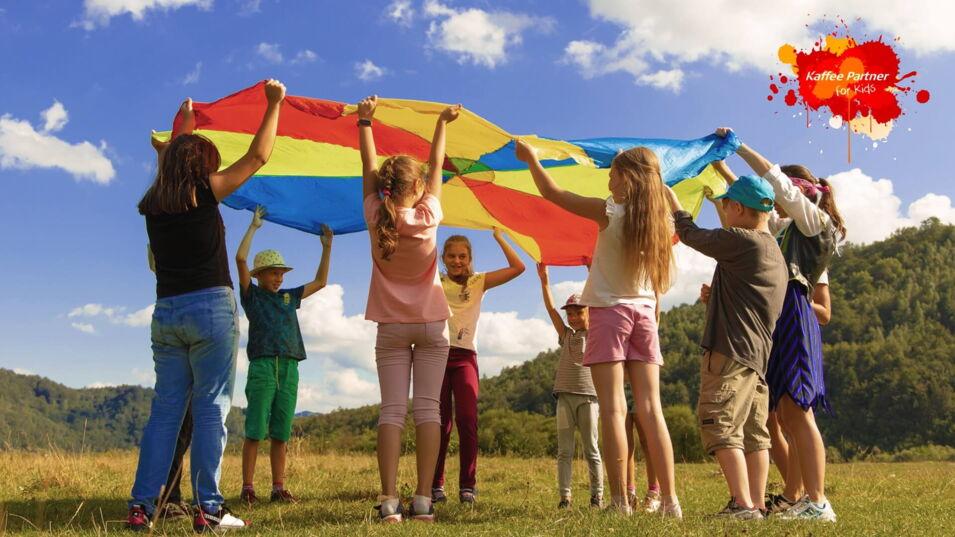 Kinder auf Wiese mit Regenbogentuch