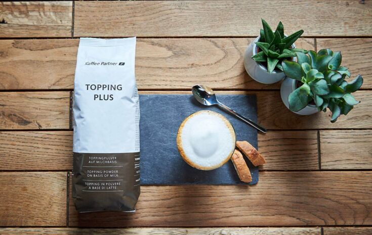 Eine Tüte Milchpulver Kaffee Partner Topping Plus liegt auf einem Holztisch