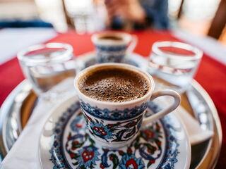 Traditioneller türkischer Kaffee in einer verzierten Tasse, serviert mit einem Glas Wasser auf einem silbernen Tablett.