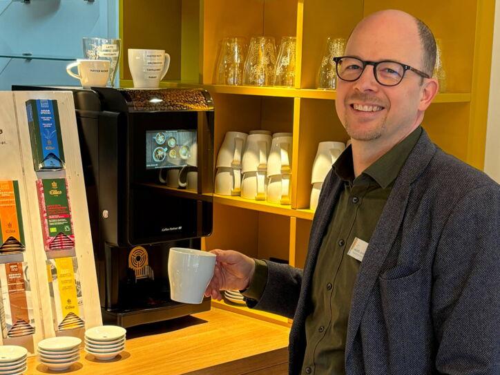 Michel Schulz, lächelnd mit einer Tasse Kaffee am Kaffeevollautomaten im City Hotel Bremerhaven