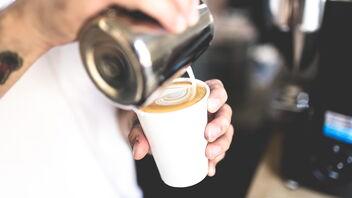 Mann macht Latte Art Herz in Becher