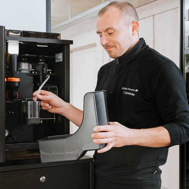 Servicetechniker führt Wartung an Kaffeevollautomat durch Techniker reinigt Teile eines geöffneten Kaffeevollautomaten im Büro