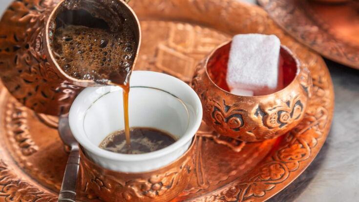 Traditioneller türkischer Kaffee wird in eine verzierte Tasse aus einem Kupfergefäß gegossen, mit einem Stück Zucker auf dem Tablett.