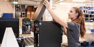 Fachkundige Technikerin klappt einen hochwertigen Kaffeevollautomaten in einer modernen Montagehalle auf.