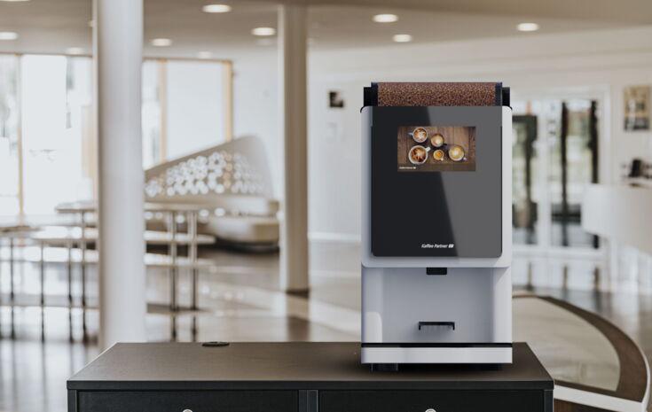 Der weiß lackierte Kaffeevollautomat BARISTA Compact steht auf einem Untertisch im Forum von Kaffee Partner
