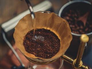 Heißes Wasser wird langsam über frisch gemahlenen Kaffee in einem Handfilter gegossen.