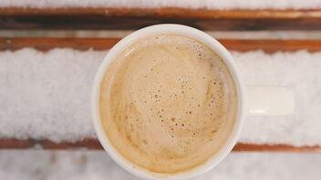 Kaffee mit Crema von oben auf einer verschneiten Parkbank